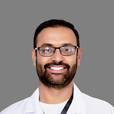 Dentist Sushen Sharma Smiling In Front Of Grey Background